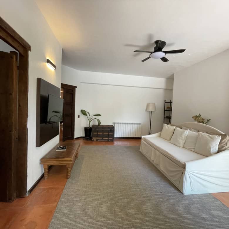 Modern living room with white sofa, ceiling fan, and wooden furniture in a bright, spacious interior.