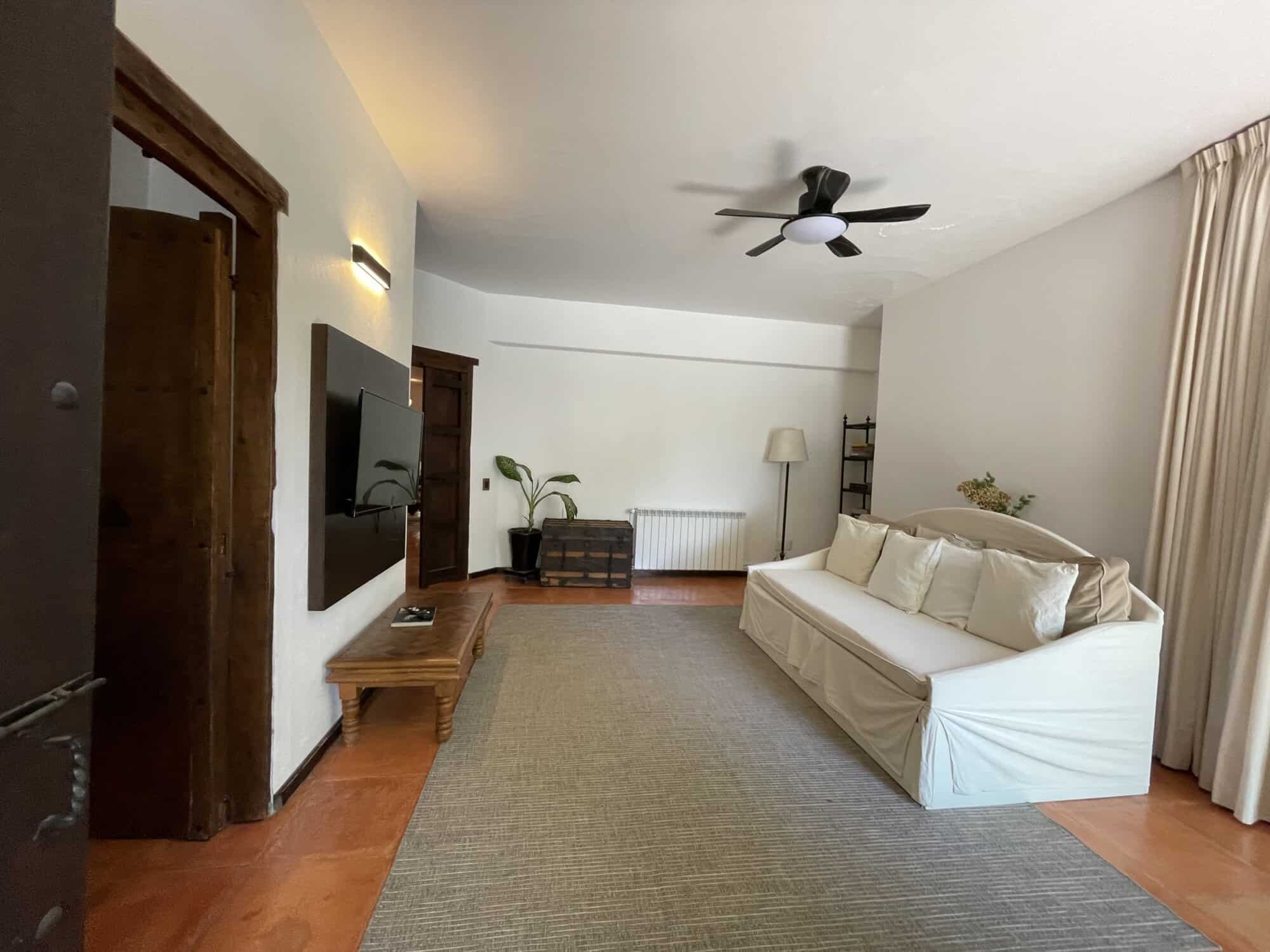 Modern living room with white sofa, ceiling fan, and wooden furniture in a bright, spacious interior.