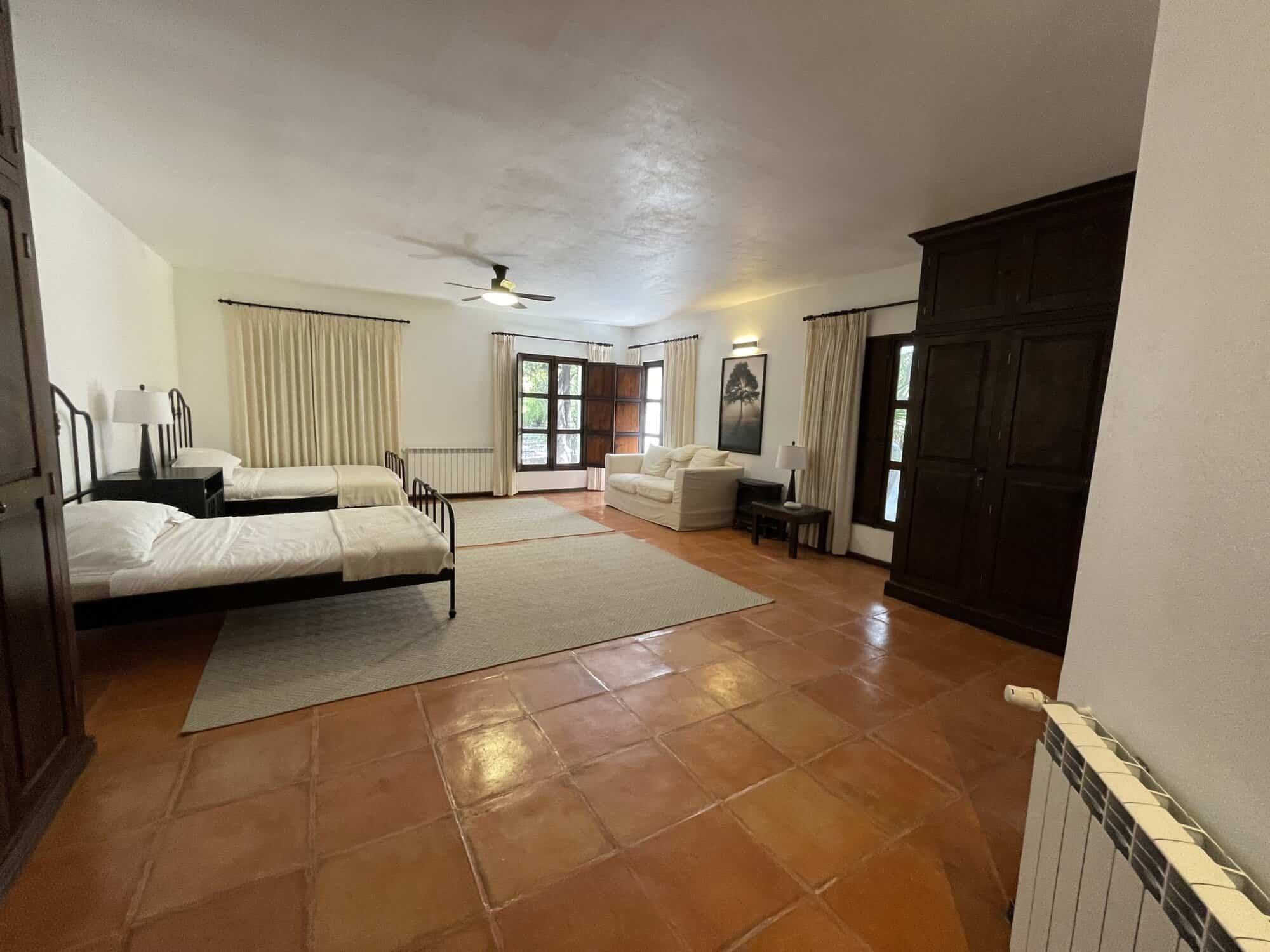 Bright bedroom with two beds, sitting area, and balcony access. Ideal for comfortable living in a sp.