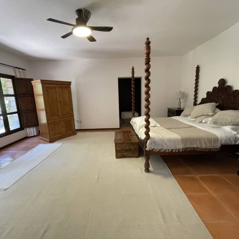 Large bedroom featuring a four-poster bed, wooden wardrobe, and natural light from windows.