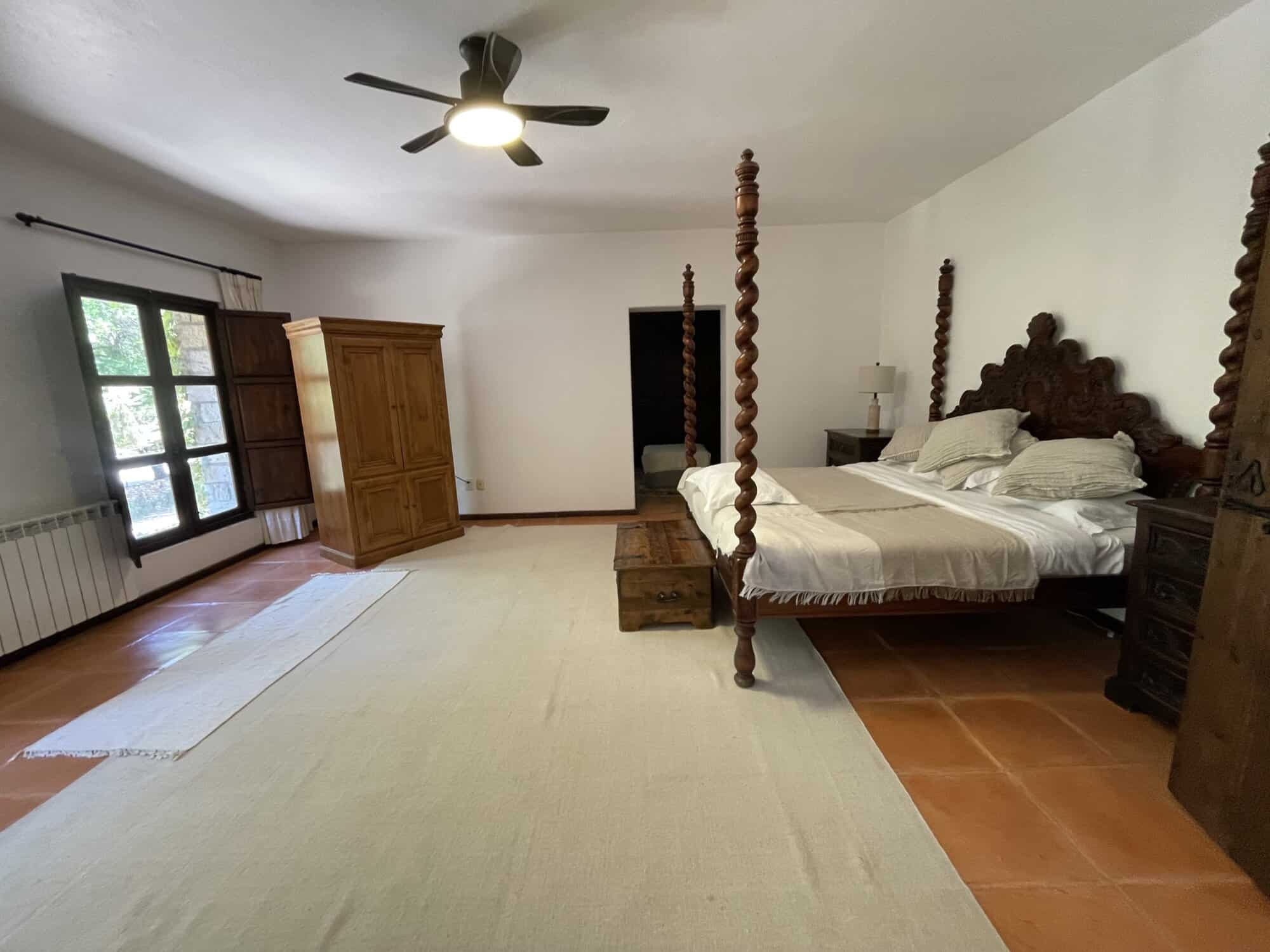 Large bedroom featuring a four-poster bed, wooden wardrobe, and natural light from windows.