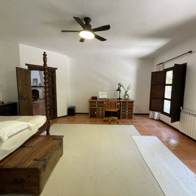 Cozy bedroom featuring wooden furniture, a large window with shutters, and a ceiling fan for comfort.