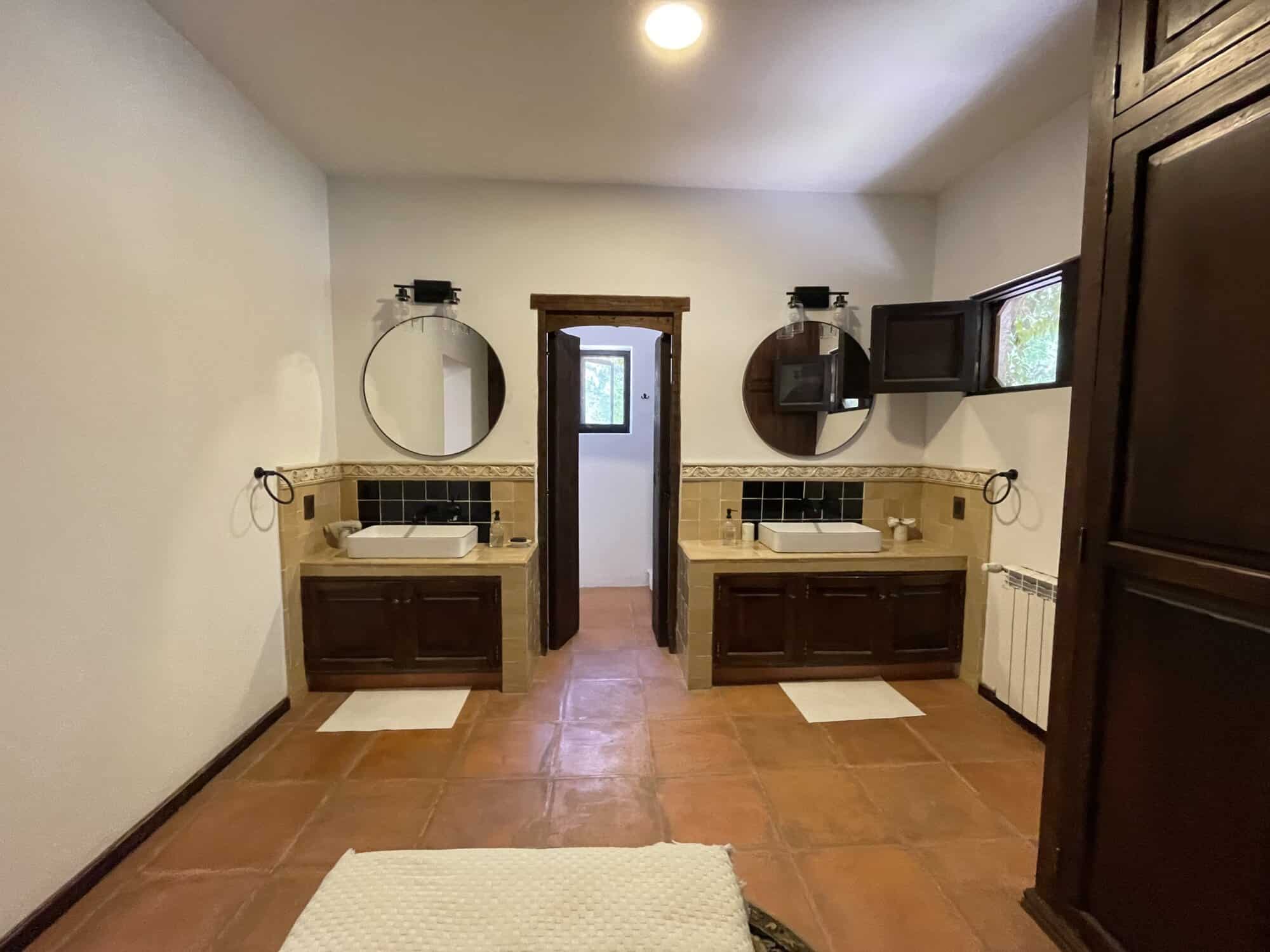 Bathroom with two sinks, round mirrors, and wooden cabinetry for a stylish look.