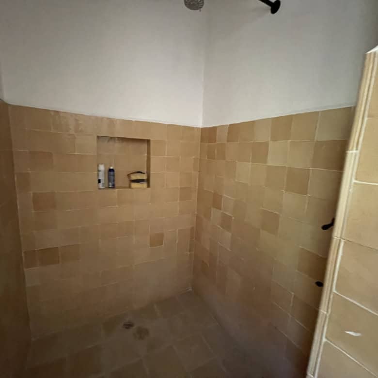 Shower area with beige tiles and built-in shelf for toiletries.