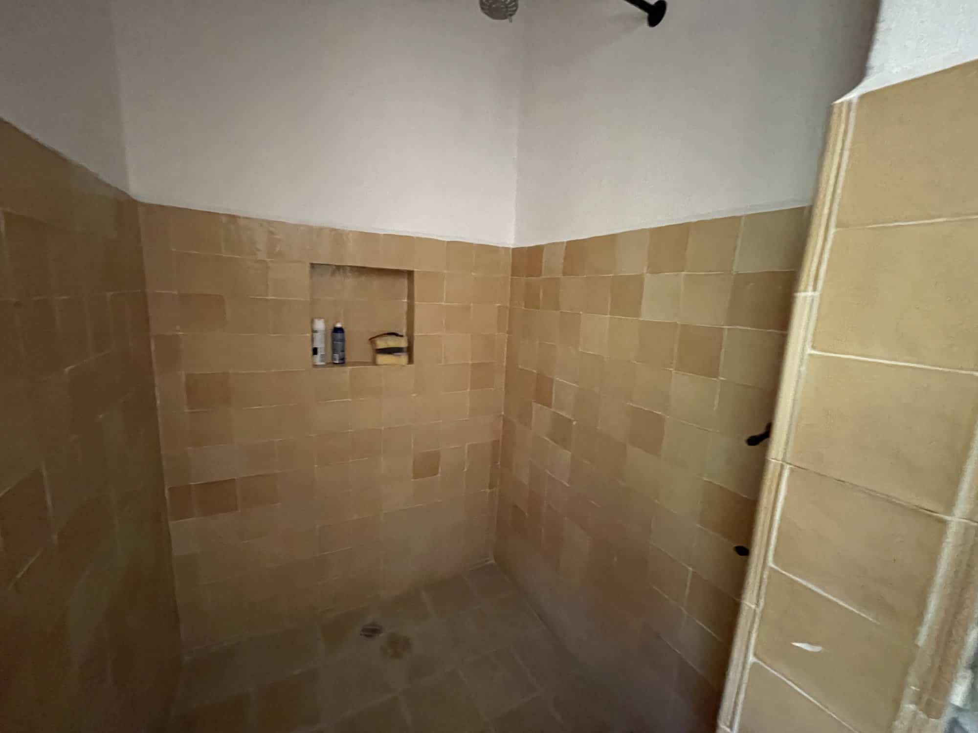 Shower area with beige tiles and built-in shelf for toiletries.