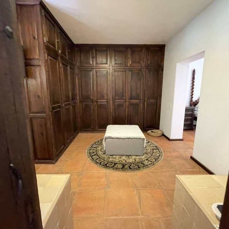 Modern wooden closet room with ample storage and a cozy ottoman in a well-lit space.