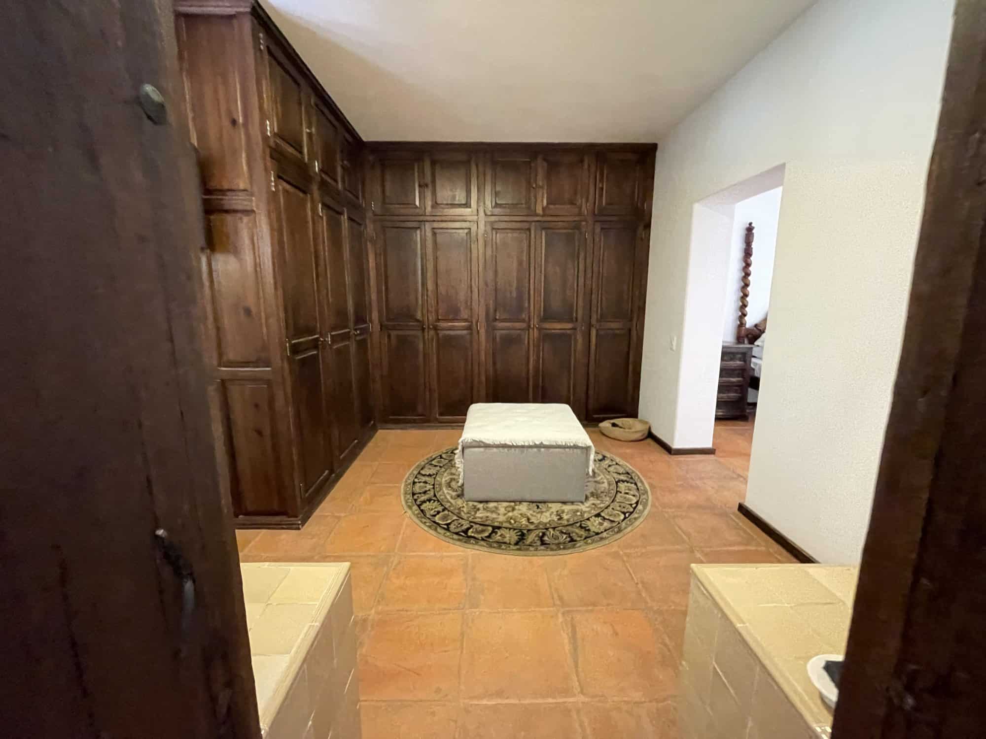 Modern wooden closet room with ample storage and a cozy ottoman in a well-lit space.