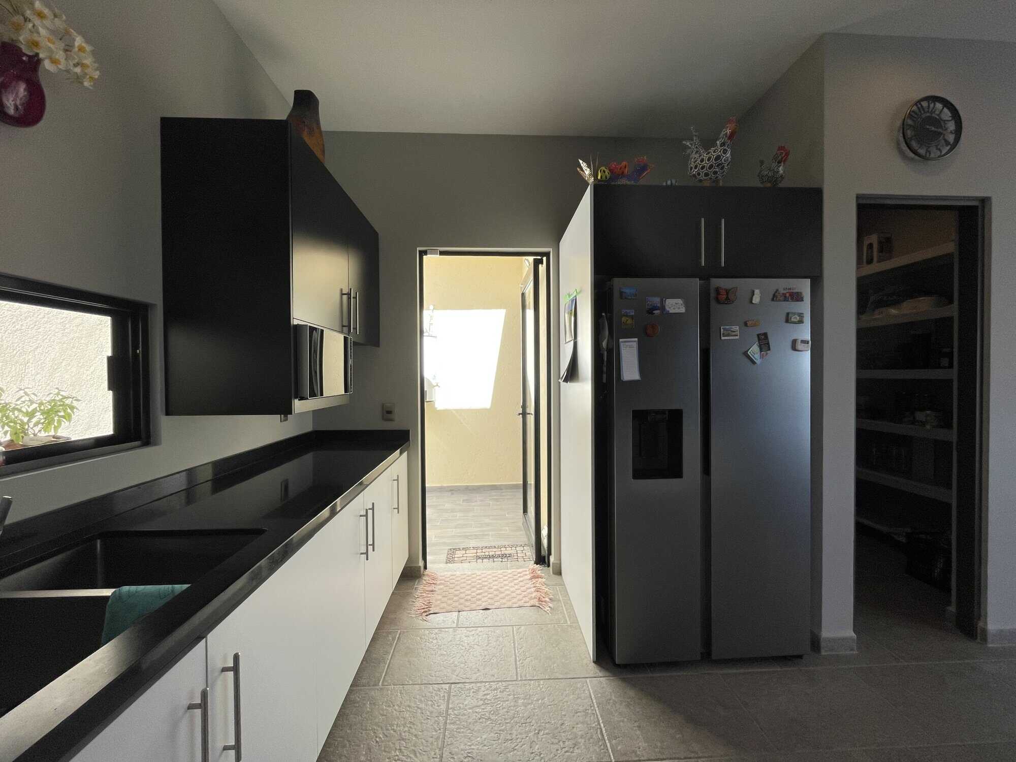 Bright kitchen with black and white cabinets, stainless steel fridge, and natural light.