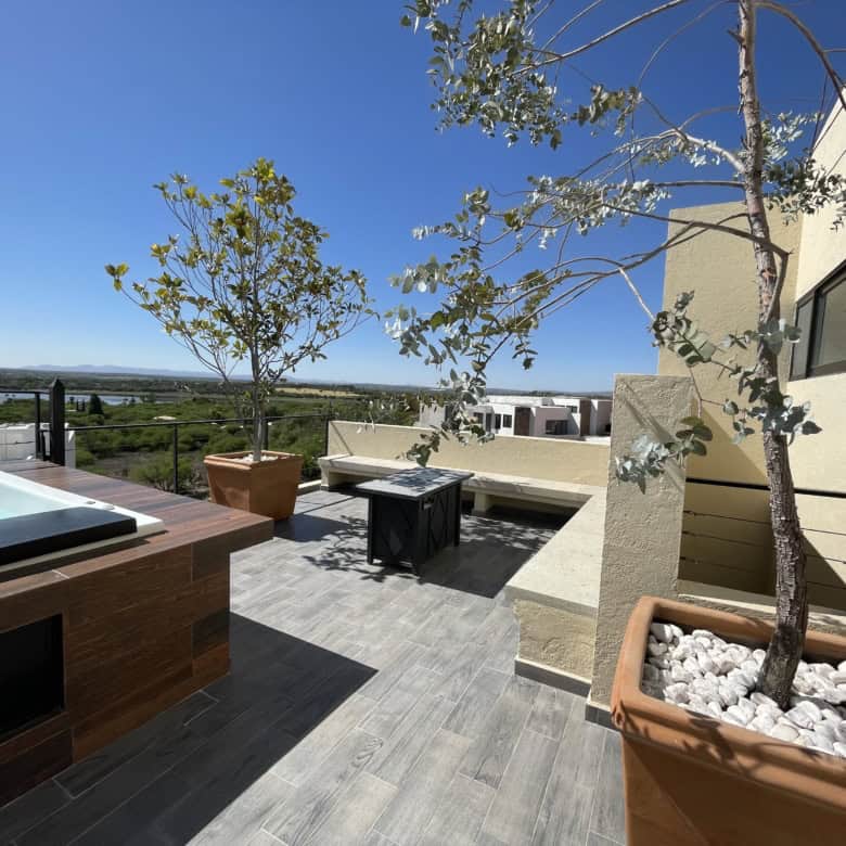 Rooftop terrace featuring modern outdoor furniture, potted trees, and scenic cityscape views under a.