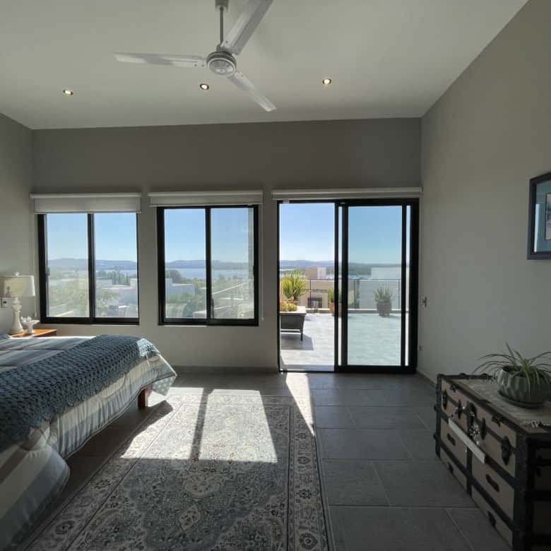 Modern bedroom with large windows and balcony overlooking scenic landscape.