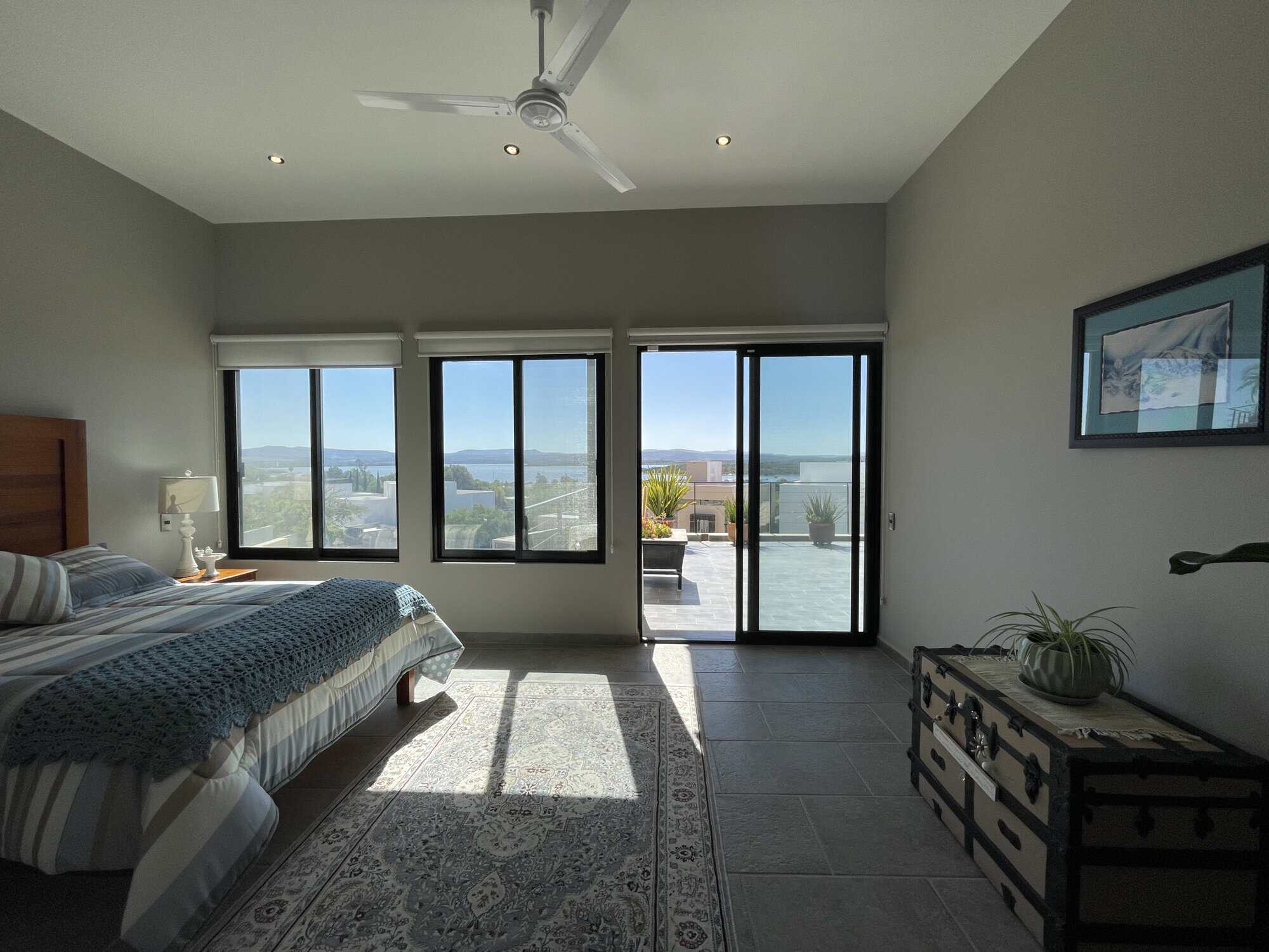 Modern bedroom with large windows and balcony overlooking scenic landscape.