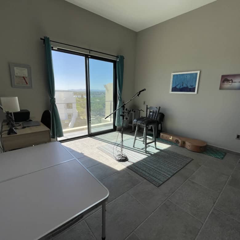 Bright room with large glass door overlooking the sea, featuring musical instruments and minimal dec.