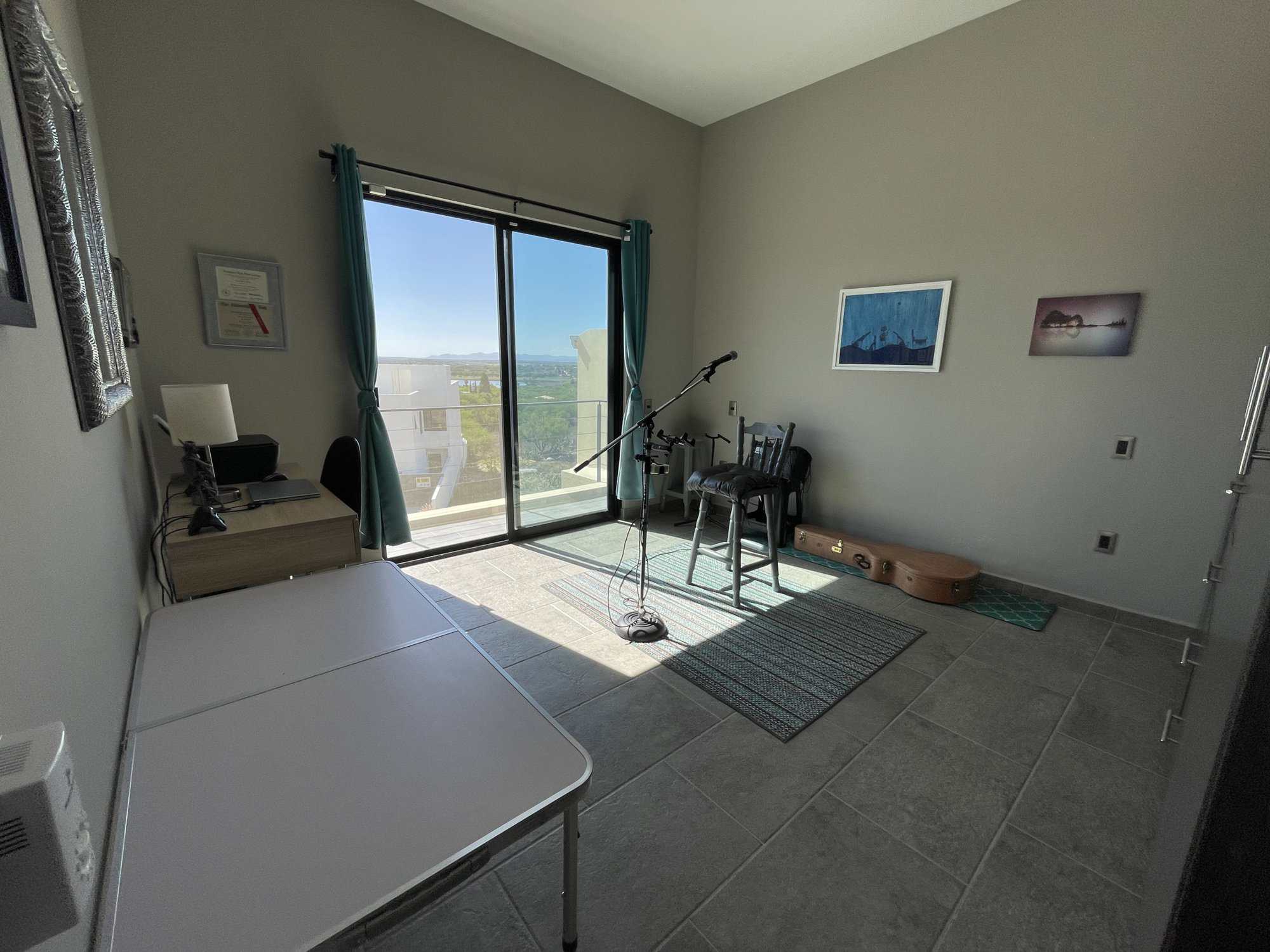 Bright room with large glass door overlooking the sea, featuring musical instruments and minimal dec.