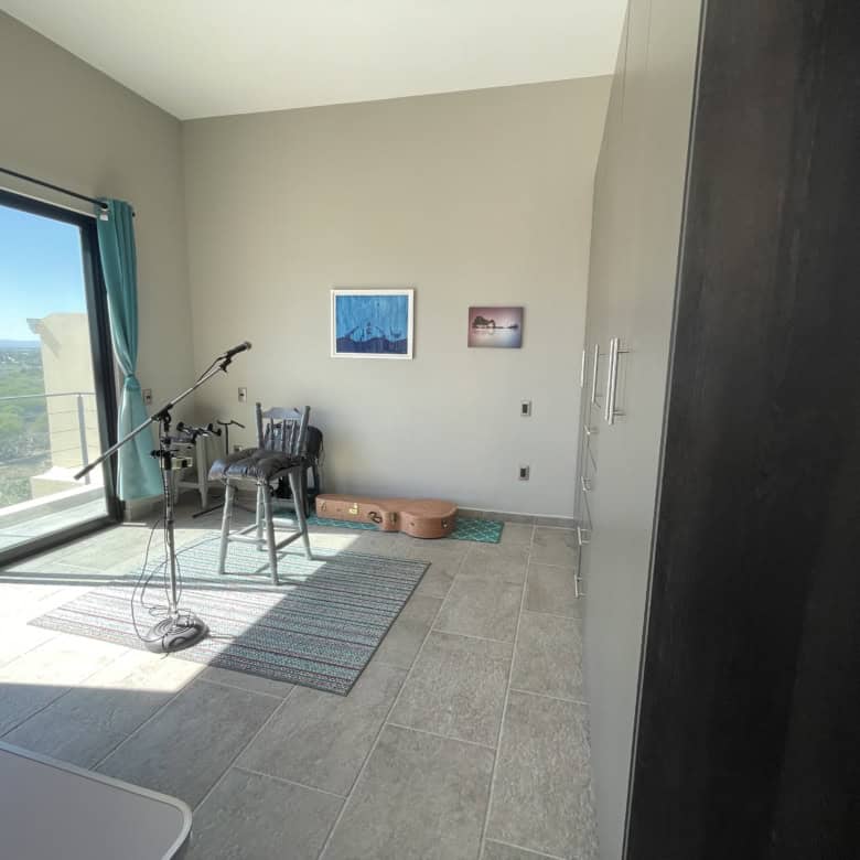 Bright room with large glass doors overlooking the ocean, featuring a telescope, chairs, and artwork.