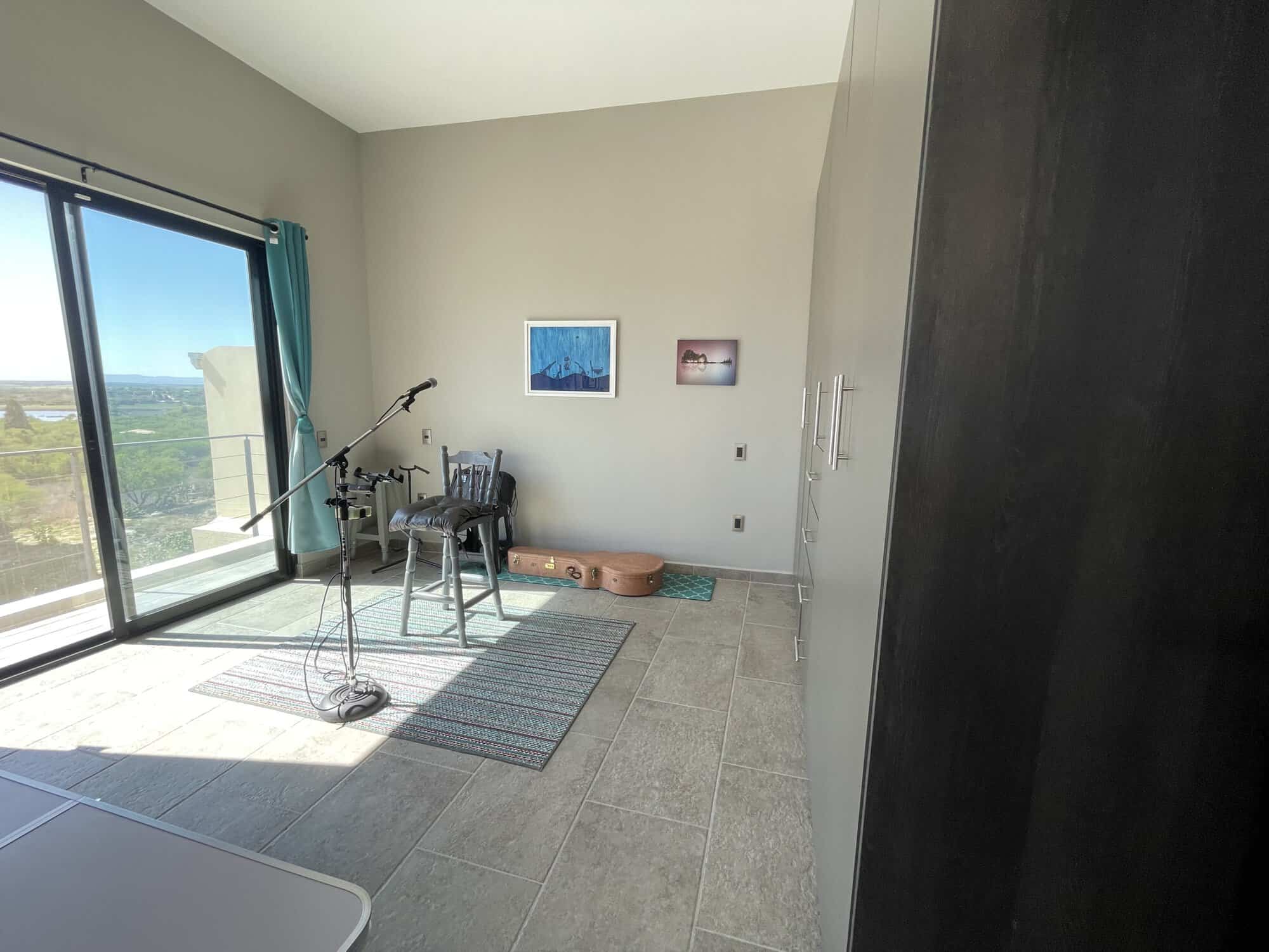 Bright room with large glass doors overlooking the ocean, featuring a telescope, chairs, and artwork.