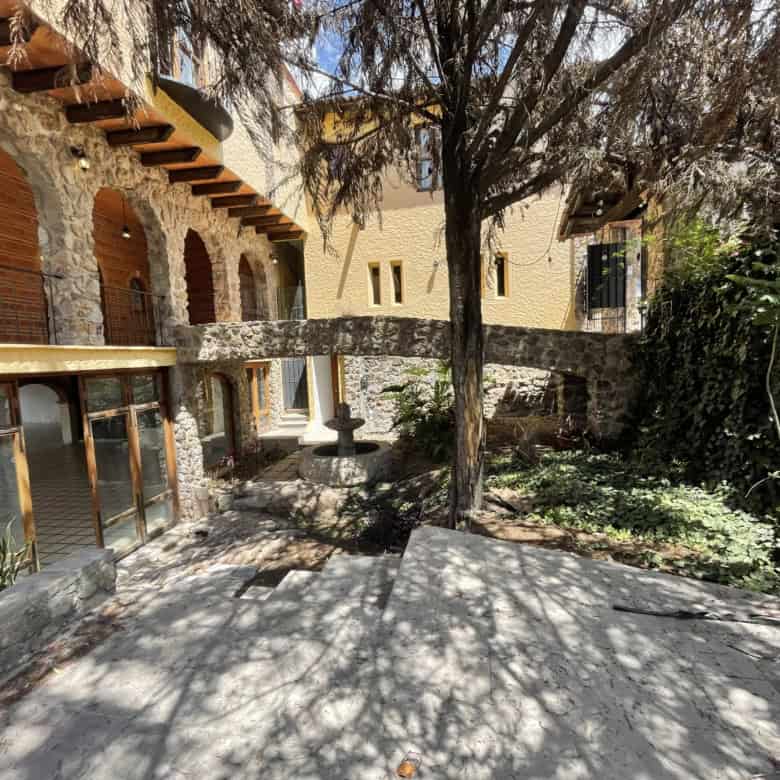 Stone house with courtyard, garden, and shaded trees in a picturesque location.