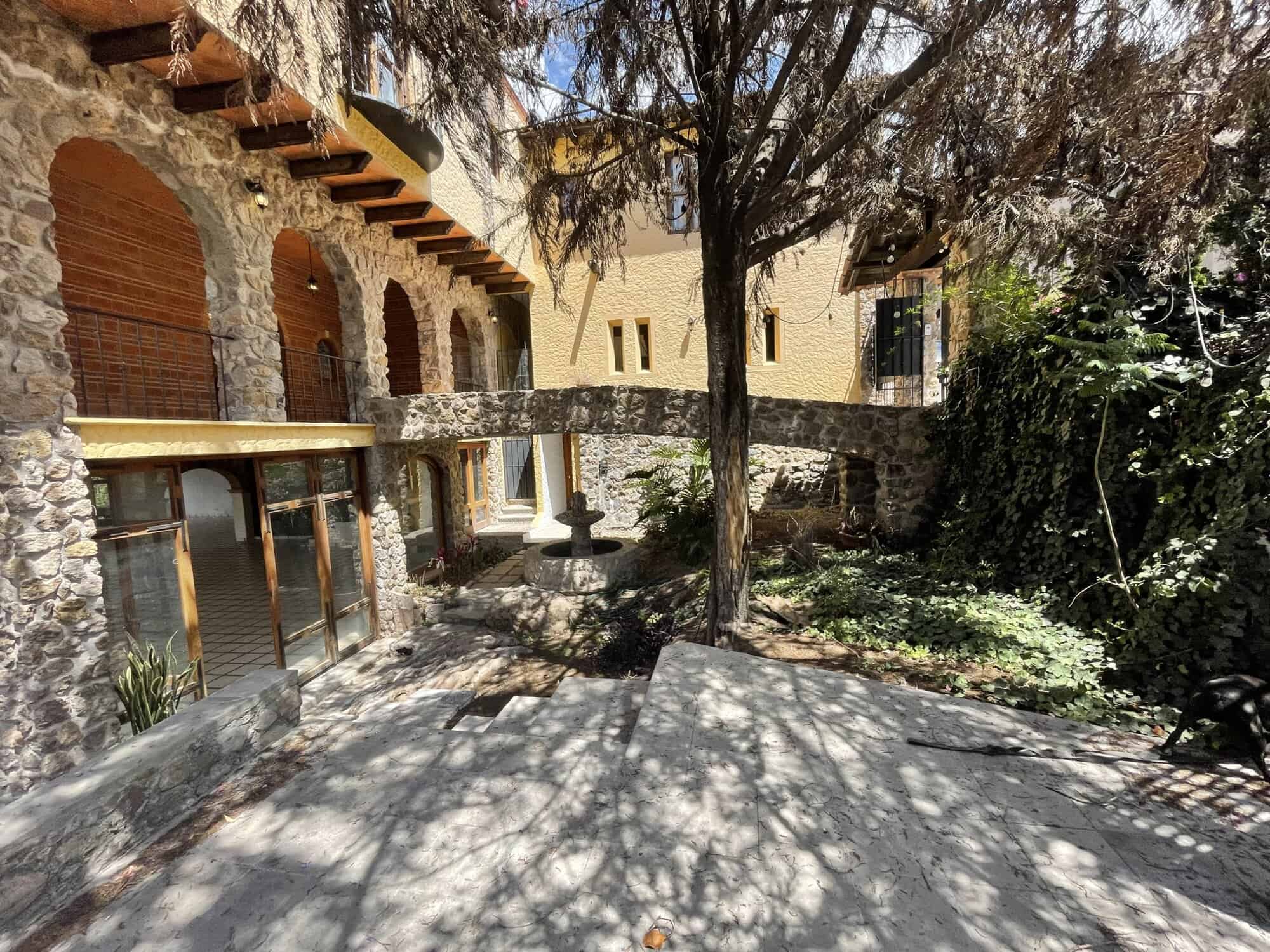 Stone house with courtyard, garden, and shaded trees in a picturesque location.