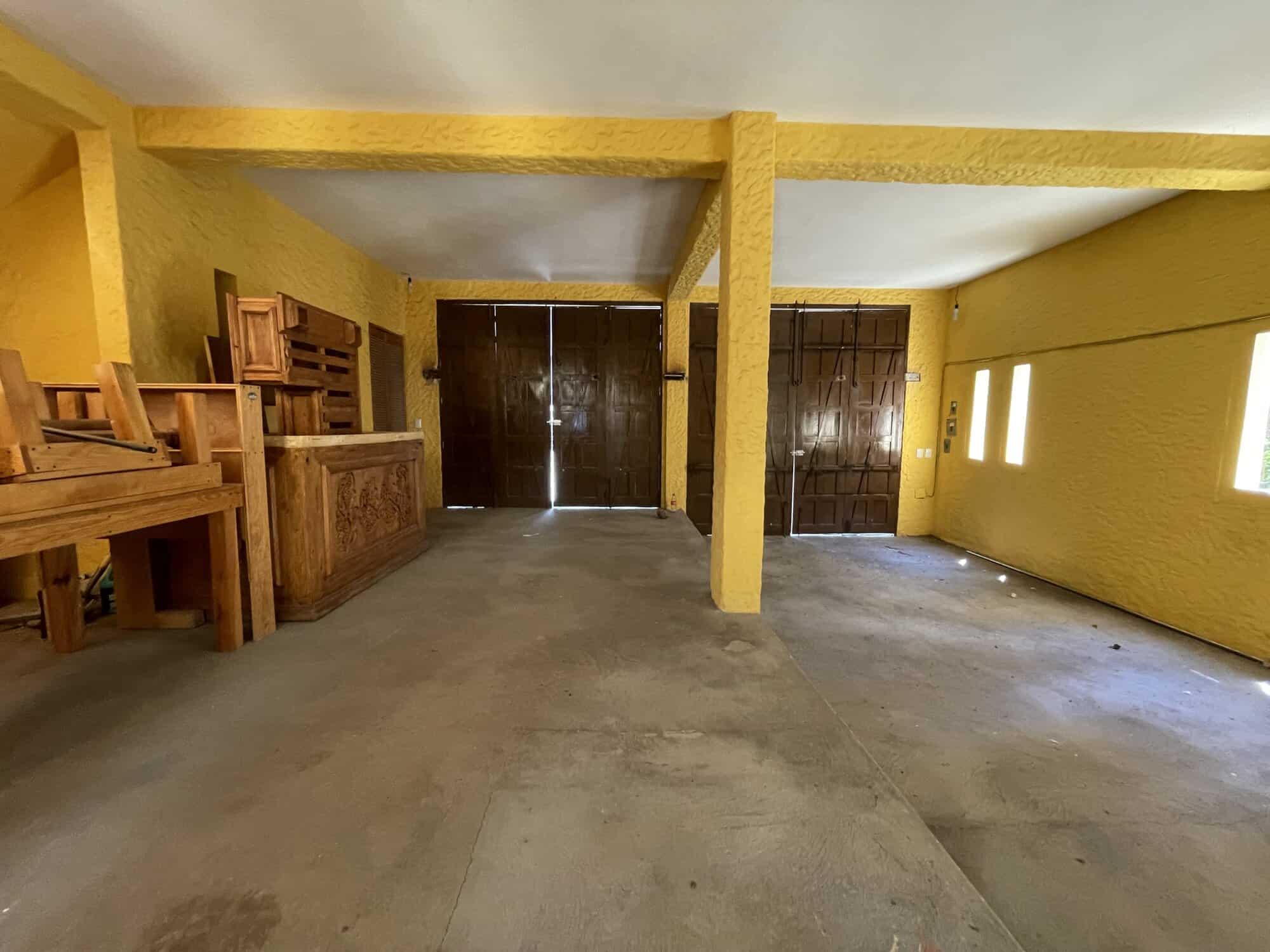 Interior of a bright yellow room with wooden furniture and large dark doors.