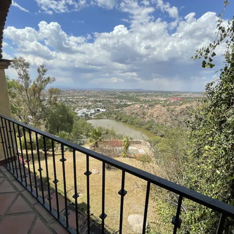 Panoramic view of river and city from balcony with lush greenery and blue sky.