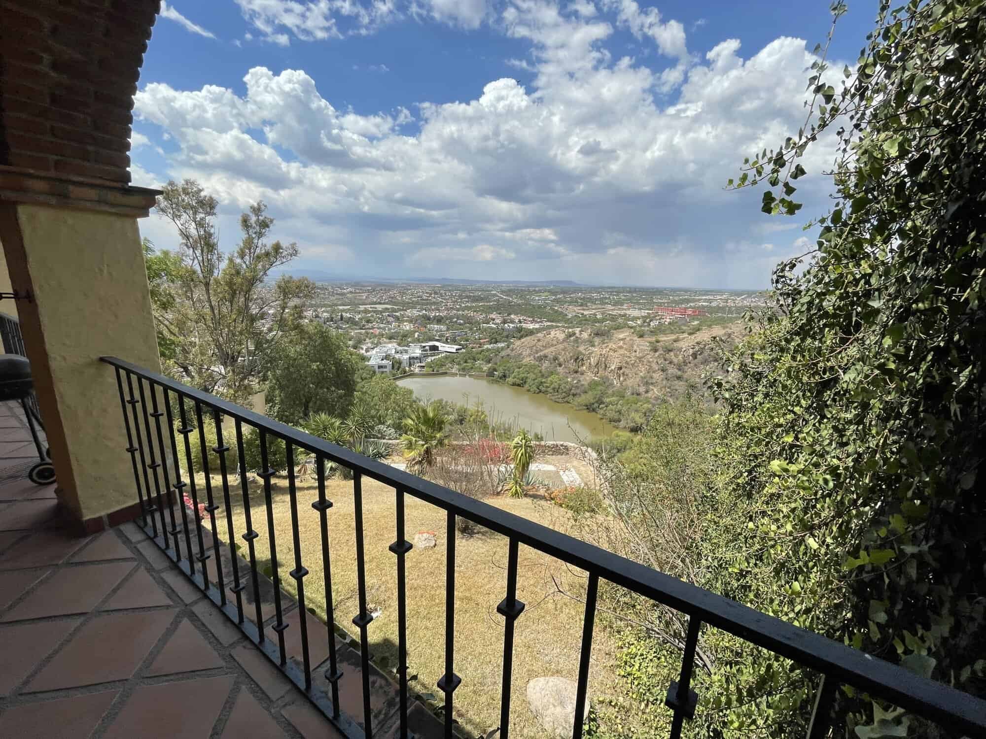 Panoramic view of river and city from balcony with lush greenery and blue sky.