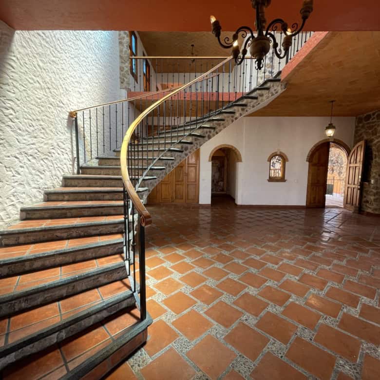 Spiral staircase leading to an upper level in a spacious, rustic interior with terracotta tile floor.