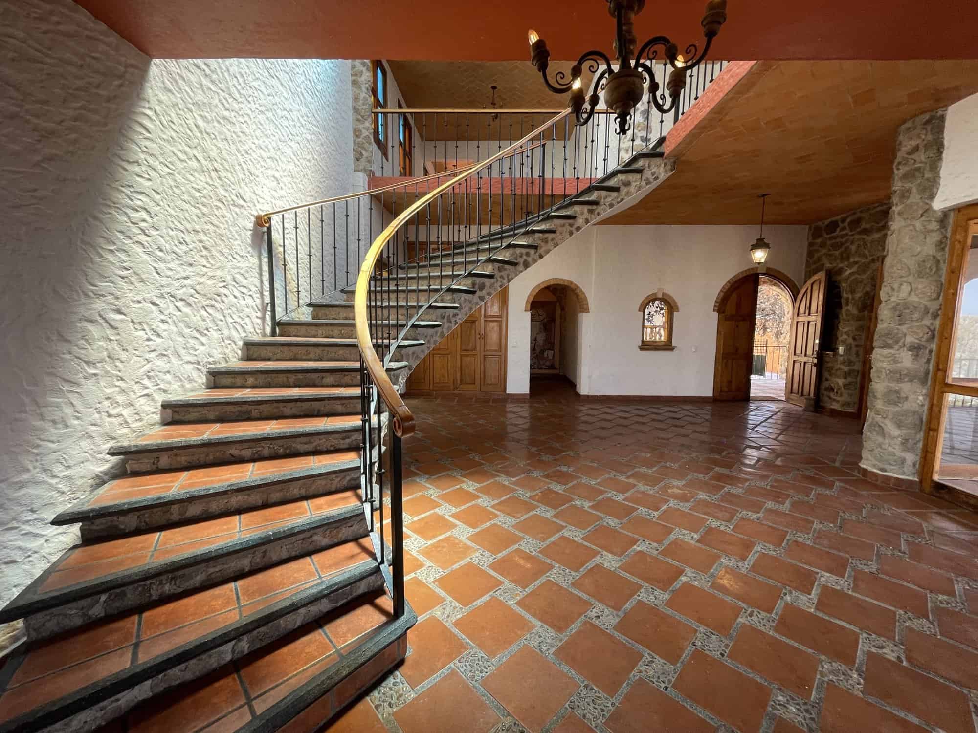 Spiral staircase leading to an upper level in a spacious, rustic interior with terracotta tile floor.
