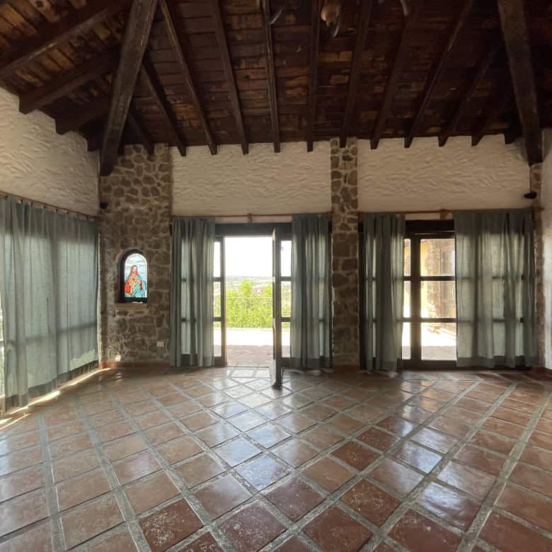 Luxury living room with stone walls, large windows, and wooden ceiling beams. Bright, spacious inter.