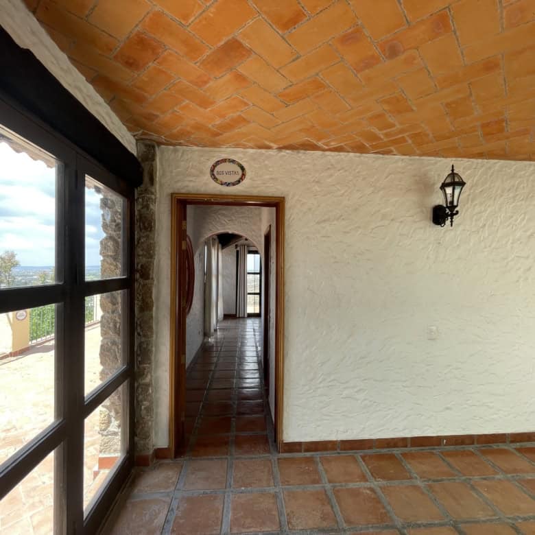 Spacious room featuring terracotta flooring, stone walls, and large windows with scenic views.