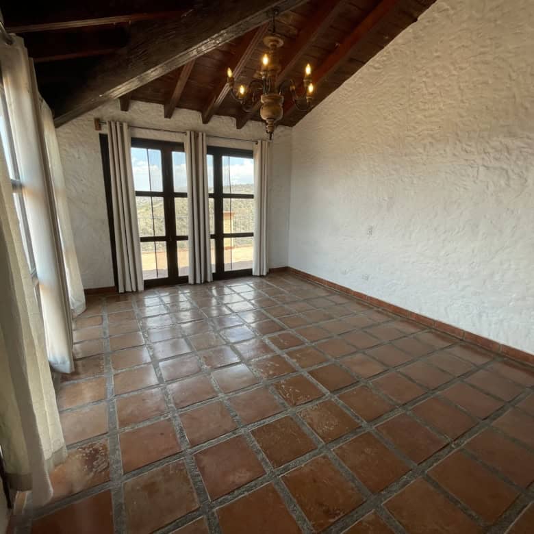 Spacious rustic living room with terracotta tile flooring and exposed wooden beams. Bright space wit.