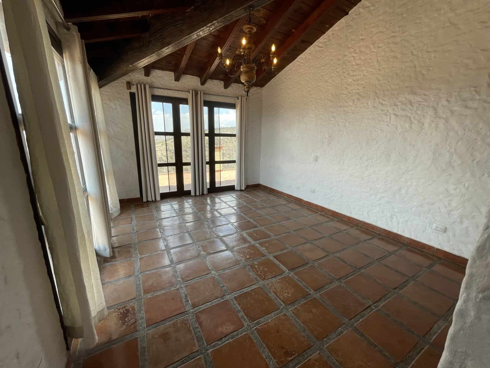 Spacious rustic living room with terracotta tile flooring and exposed wooden beams. Bright space wit.