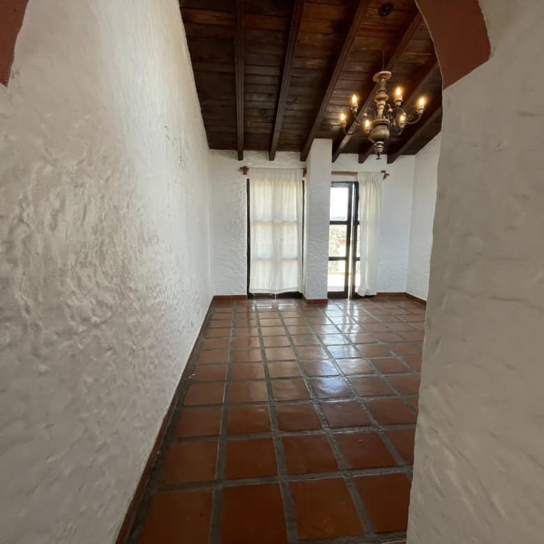 Elegant interior featuring white textured walls, terracotta tiled flooring, and wooden ceiling beams.