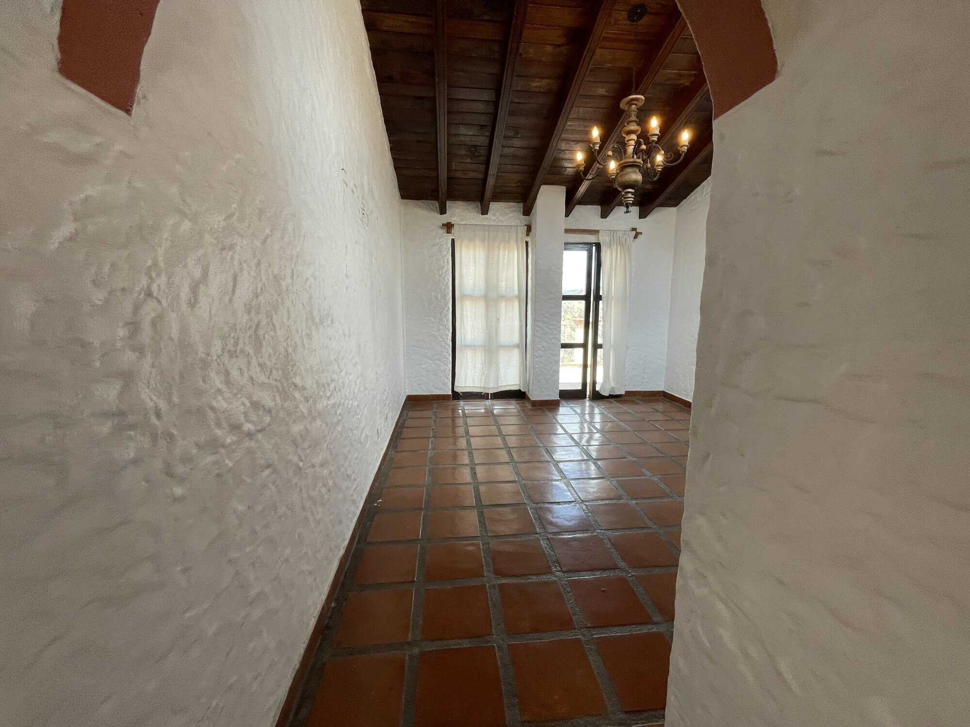 Elegant interior featuring white textured walls, terracotta tiled flooring, and wooden ceiling beams.