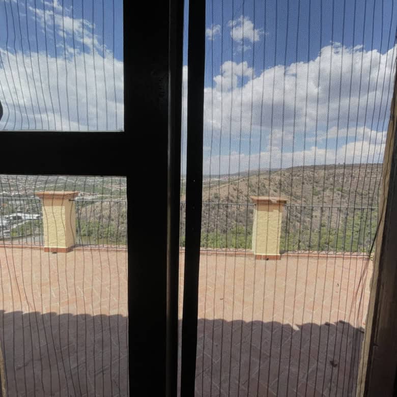 Balcony view overlooking mountains and sky with clouds, framed by glass doors.