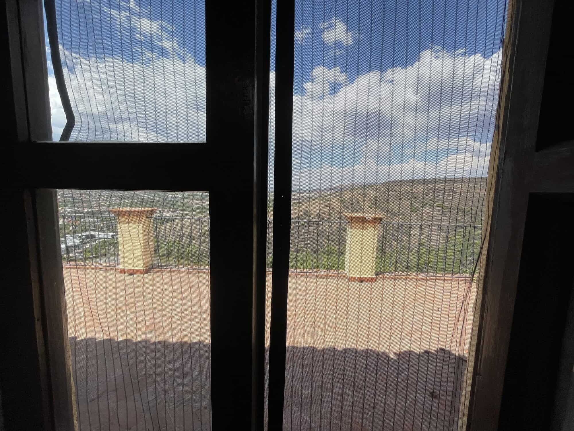 Balcony view overlooking mountains and sky with clouds, framed by glass doors.