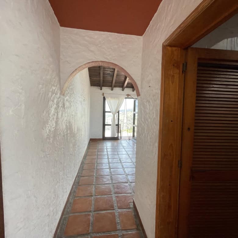 Spacious hallway inside a Spanish-style house with terracotta tiles and white textured walls.