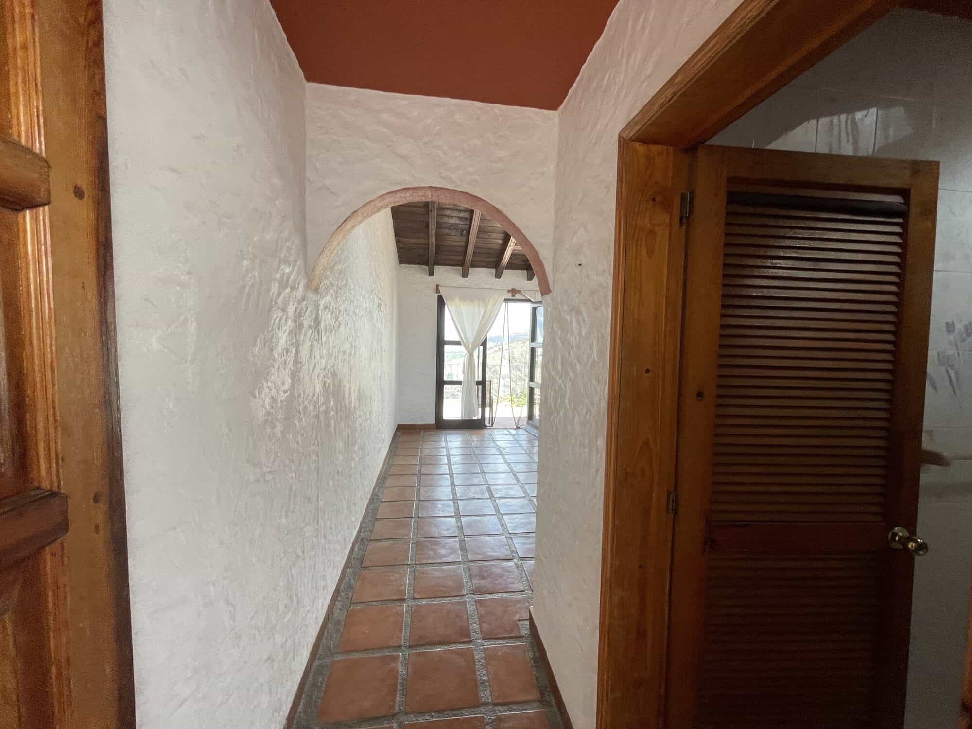 Spacious hallway inside a Spanish-style house with terracotta tiles and white textured walls.