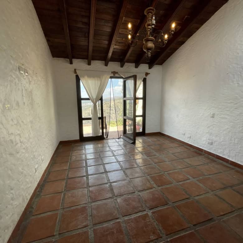 Bright room with balcony and scenic views, featuring rustic terracotta tiles and wooden ceiling beam.
