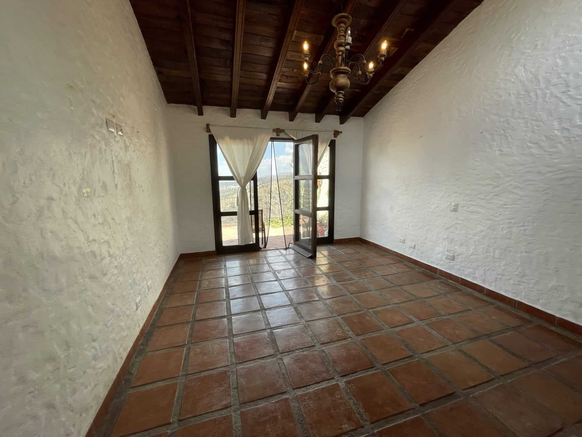 Bright room with balcony and scenic views, featuring rustic terracotta tiles and wooden ceiling beam.