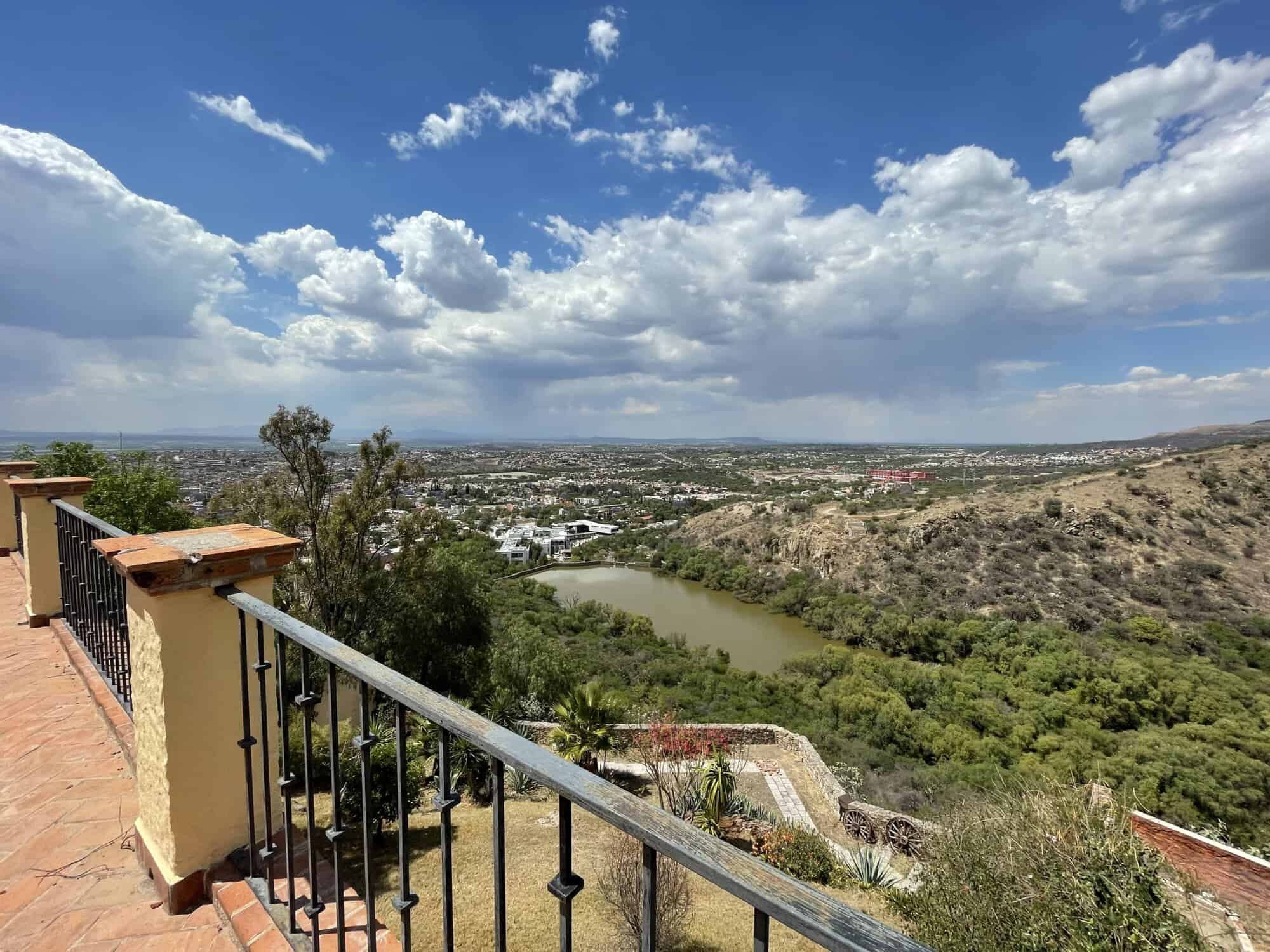 Panoramic view of a river flowing through lush green hills and a distant city skyline under a partly.