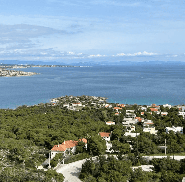 Beach view of Chamolia in Athens with lush greenery and the Aegean Sea in the background.