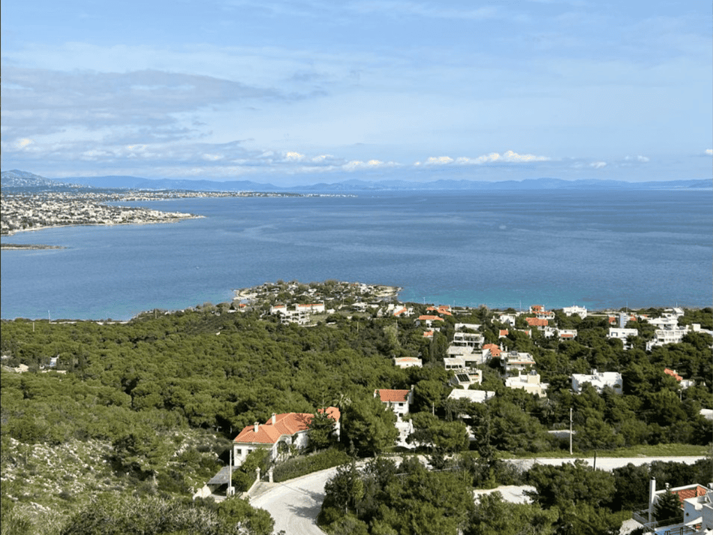 Beach view of Chamolia in Athens with lush greenery and the Aegean Sea in the background.