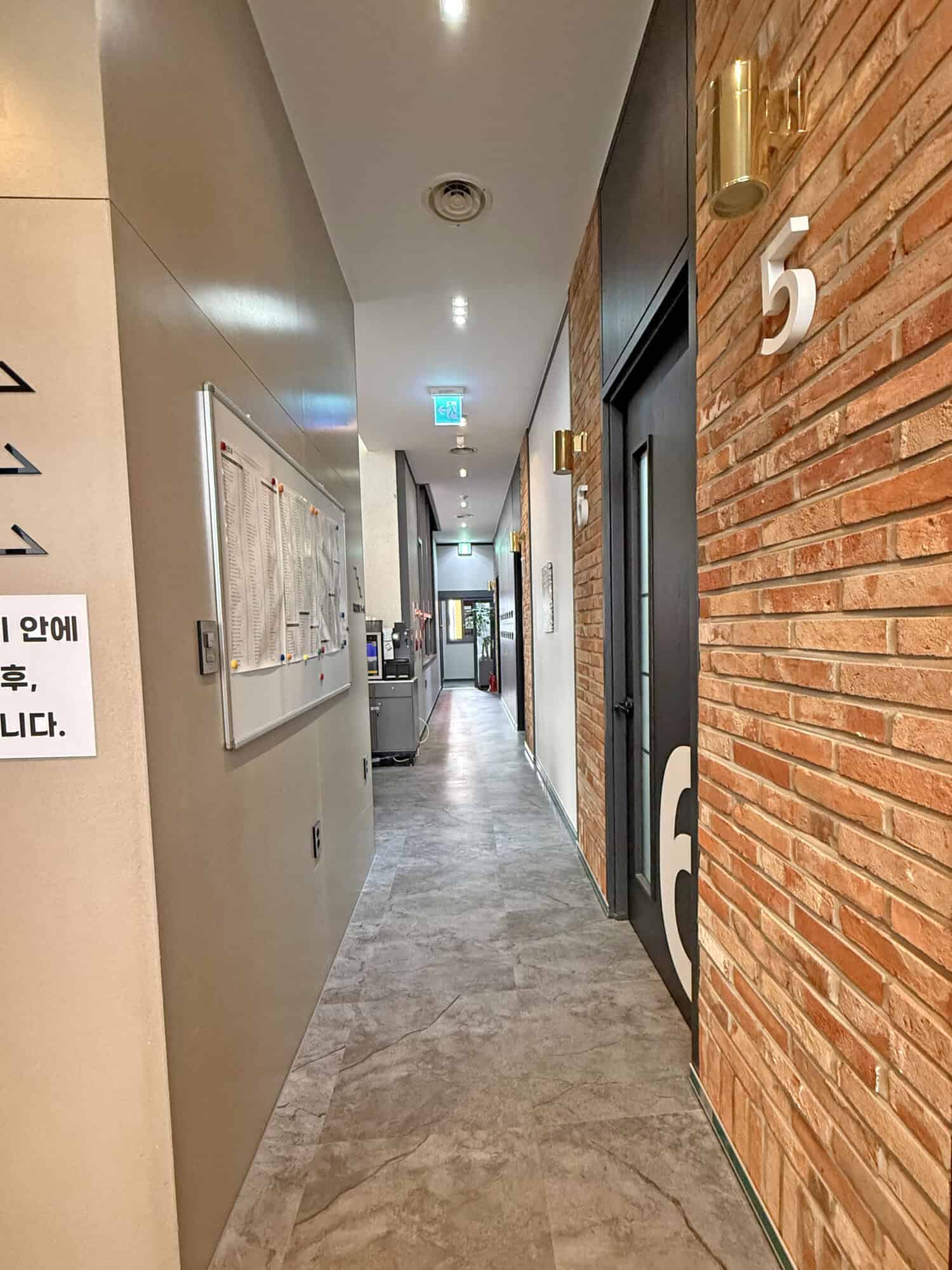 Hotel corridor with brick wall, numbered door 5, and modern lighting fixtures.