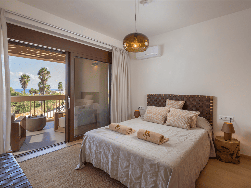 Comfortable bedroom at Maleme Residences with balcony views of palm trees and the sea. Perfect for r.