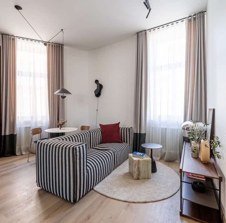 Modern living room in Riga with striped sofa, large windows, and cozy decor.