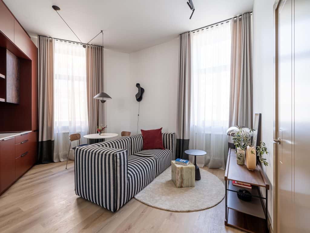 Modern living room in Riga with striped sofa, large windows, and cozy decor.