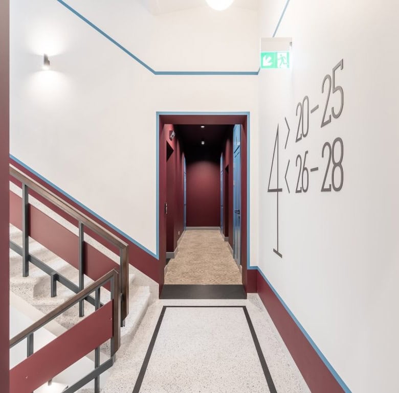 Bright, clean corridor with clear room number markings and safety exit sign.