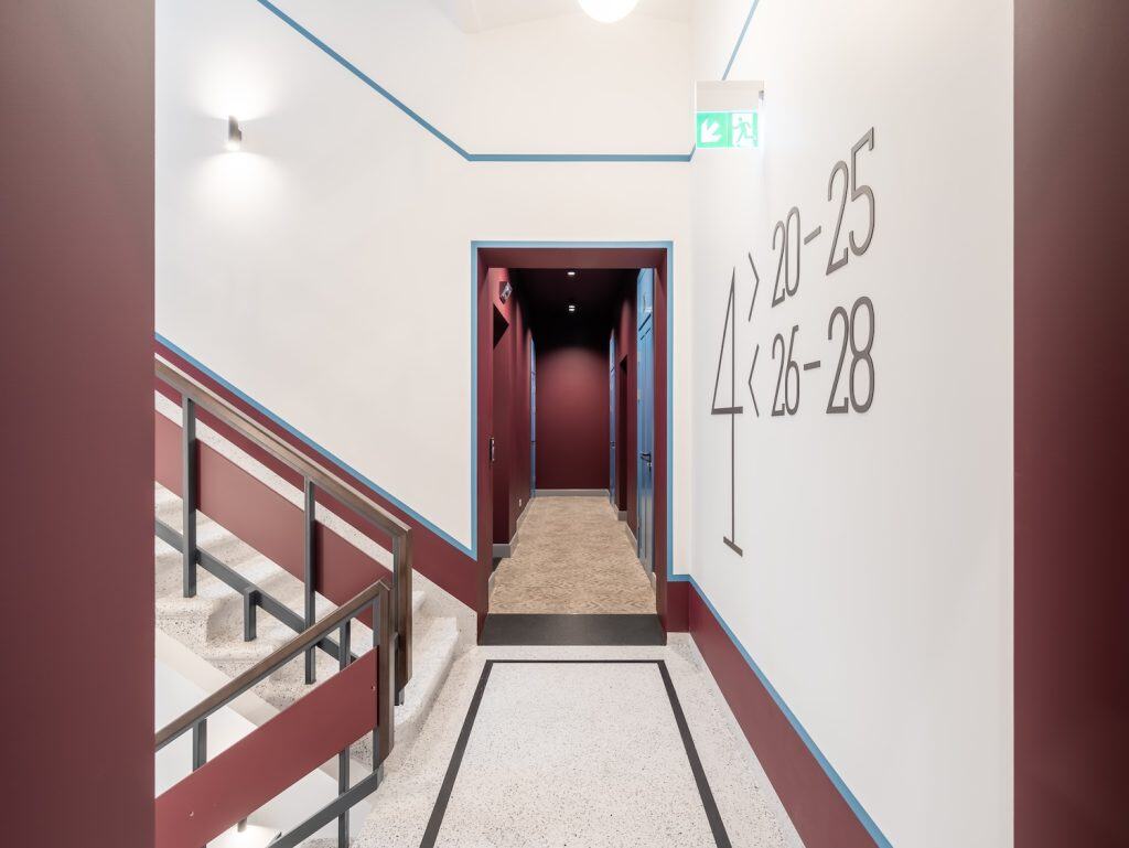 Bright, clean corridor with clear room number markings and safety exit sign.