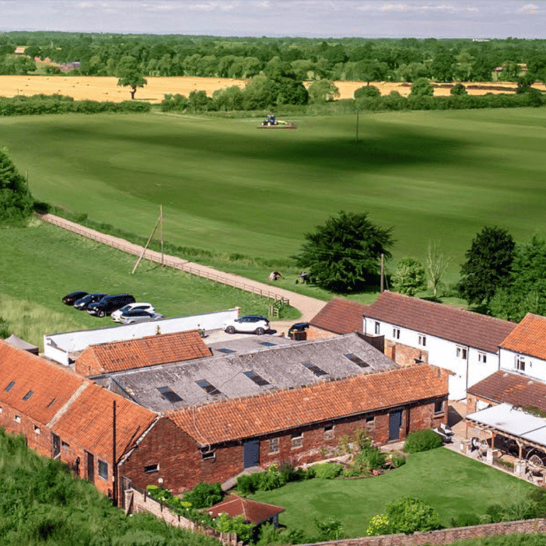 Aerial view of a spacious rural farmhouse surrounded by lush green fields and open countryside.