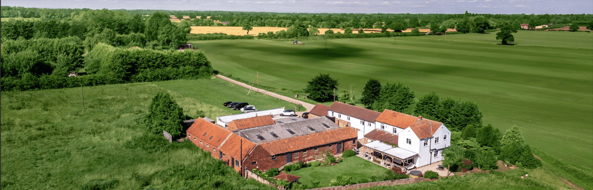 Charming Rural Farmhouse with Land for Sale Aerial view of a spacious rural farmhouse surrounded by lush green fields and open countryside.