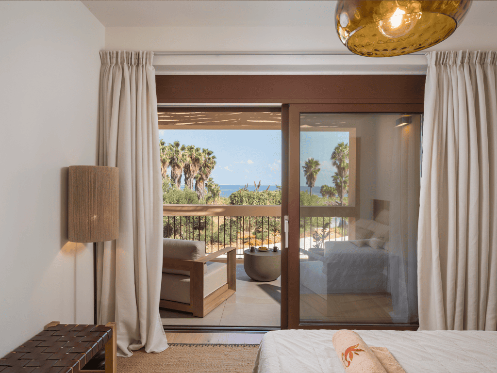 Beautiful bedroom with balcony view of palm trees and ocean in Crete.